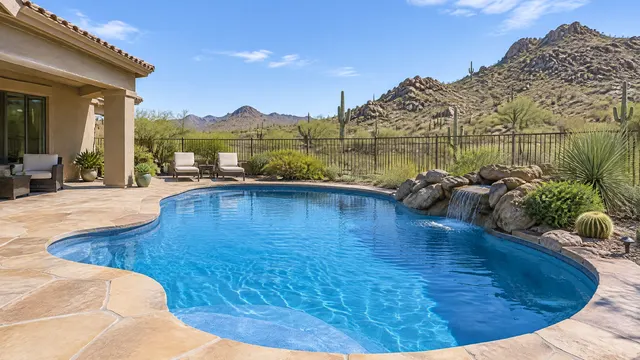 Backyard pool at a 2000s stucco home in Sonoran Foothills, far north Phoenix: curved pool with a fresh medium-blue finish, flagstone deck, view over a view-fence to rocky desert foothills dotted with saguaros