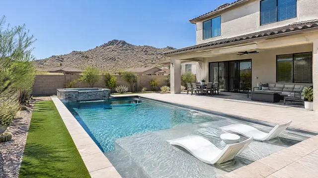 Newer two-story stucco home backyard in Stetson Valley, northwest Phoenix: geometric pool with a baja shelf, light gray finish, artificial turf strip, low desert hills in the distance