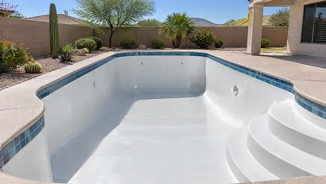 Empty residential pool in a Phoenix backyard just after new white plaster was troweled: smooth, even, damp white surface on walls and floor, clean steps, tile line intact, desert landscaping and a block wall around the yard