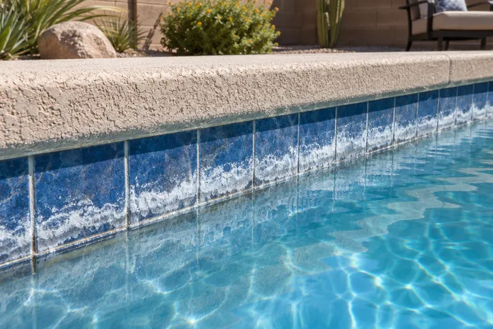Pool waterline tile crusted with white calcium scale deposits and stains just above the water
