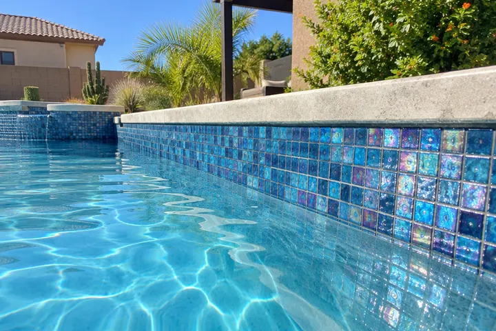 New iridescent blue glass mosaic waterline tile on a pool wall, shining in the sun